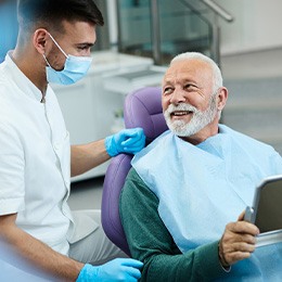 Senior patient looking at dentist while holding small mirror