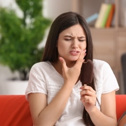 Woman sitting on couch holding her cheek in pain