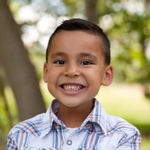 Young boy grinning outdoors after seeing children's dentist in Nepean