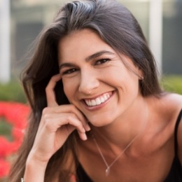 Woman in black tank top grinning with flowers in background