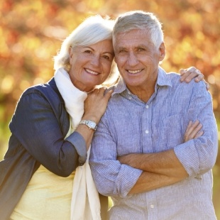 Older man and woman smiling outdoors with dental implants in Nepean