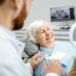 Senior woman in dental chair looking at her smile in a mirror