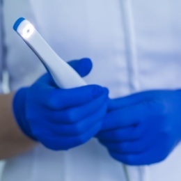 Two gloved hands holding a thin white intraoral camera