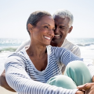 Man and woman sitting on beach and smiling with dentures in Nepean