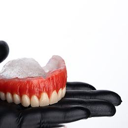 Gloved hand holding wax dentures