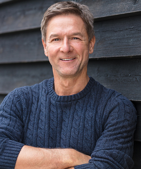 Man in dark blue sweater smiling with his arms crossed
