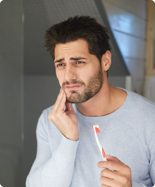 Man holding a bloody toothbrush and touching his cheek in pain