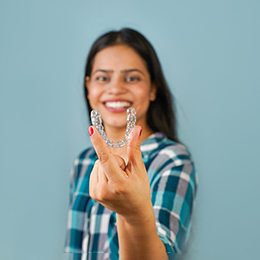 Woman in plaid shirt smiling while holding Invisalign aligner