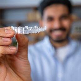 Closeup of smiling patient holding Invisalign aligner