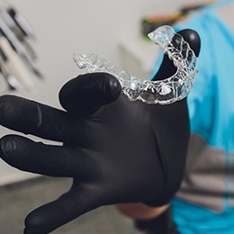 Dentist holding Invisalign aligner with black glove