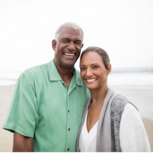 Man and woman smiling on beach after replacing missing teeth in Nepean