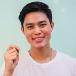 Smiling young man holding an Invisalign clear aligner