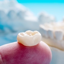 Close up of a person holding a dental crown on their finger