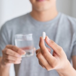 Person holding a white pill and a glass of water