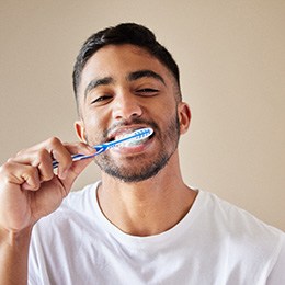 Smiling patient in white shirt brushing their teeth
