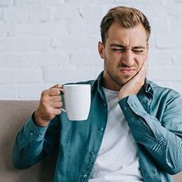 A young man holding a coffee cup and suffering a toothache