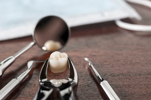 Forceps holding wisdom tooth while lying between other dental instruments